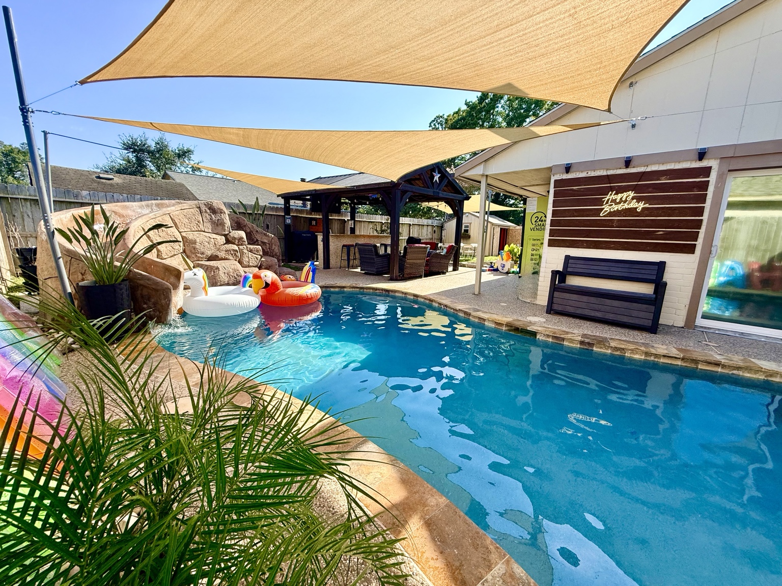 Wide view of the birthday-ready pool, shade sails, pavilion and Happy Birthday wall