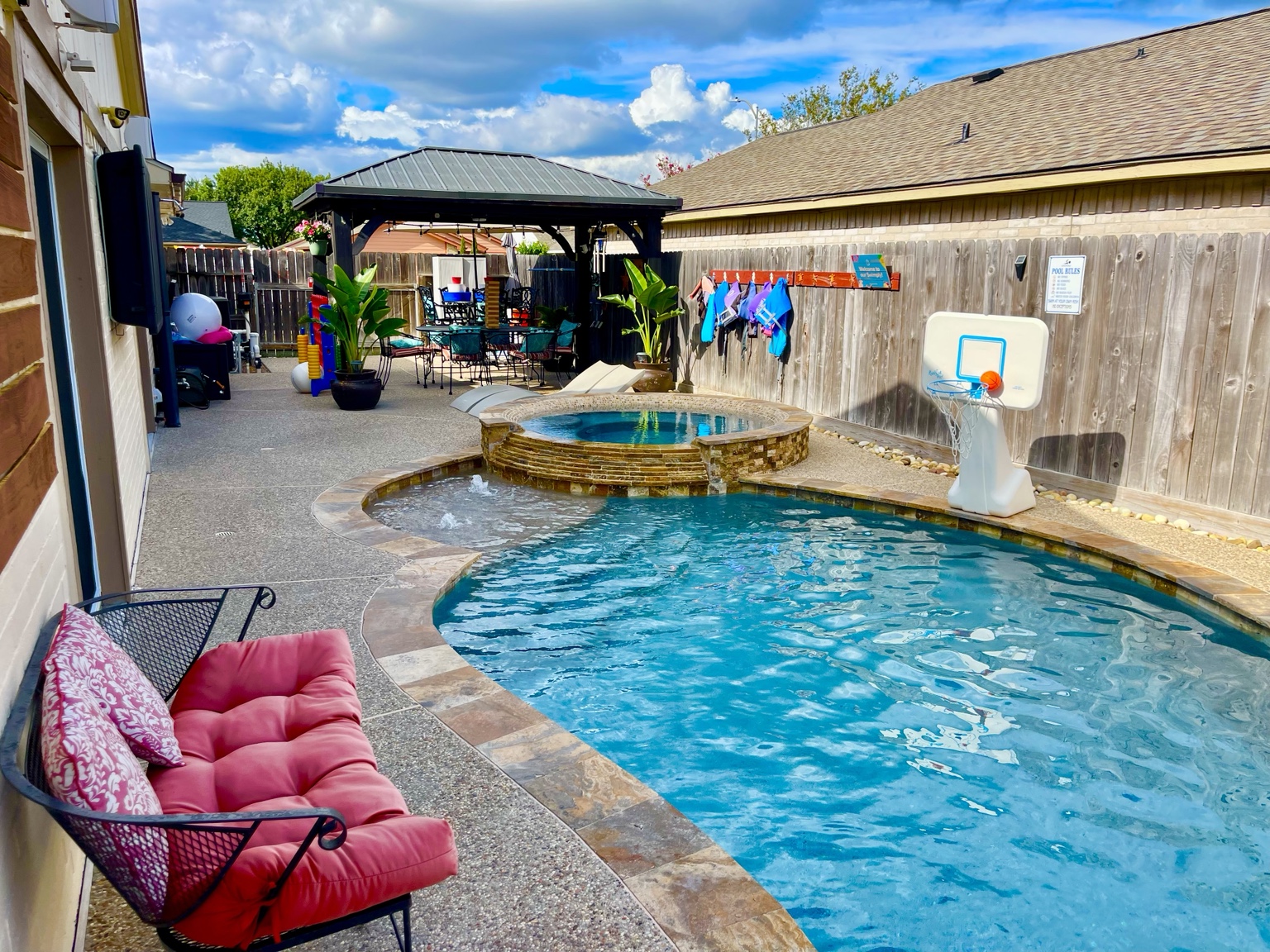 Bright pool, hot tub, basketball hoop, and covered seating